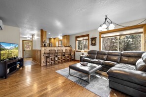 A living room with a leather sofa, wooden floor, and a TV. - 3 Bedroom Cabin, Mountain & Lake Views, Glacier (Bigfork)