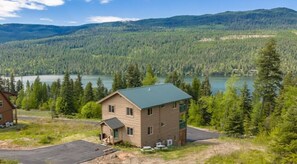 A two-story building with a green roof, surrounded by a forested area and a lake. - 3 Bedroom Cabin, Mountain & Lake Views, Glacier (Bigfork)