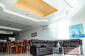 A modern living room with a sectional sofa, dining table, chairs, and a kitchen area in the background. - Casa Postal (Puerto Peñasco)