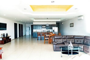 A modern living room with a leather sofa, a glass coffee table, and a dining area with wooden chairs and a kitchen in the background. - Casa Postal (Puerto Peñasco)