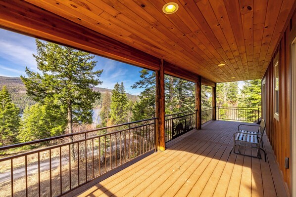 Eine Holzterrasse mit Geländer, einer Sitzbank und Blick auf einen Wald und Berge.