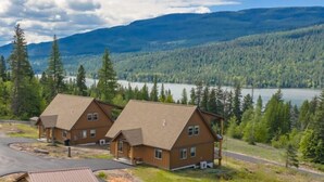 Två stugor av trä med utsikt över en sjö och skogbeklädda berg.