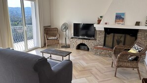 A living room with a sofa, a television, a fireplace, and a balcony with a view. - Vacation Rental 8-minute walk from the ocean - top floor of a villa (ROQUEBRUNE SUR ARGENS)