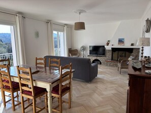A dining area with wooden chairs and a table, a living room with a sofa and TV, a fireplace, and a balcony with a view. - Gîte 500m from the sea in Les Issambres - first floor (ROQUEBRUNE SUR ARGENS)