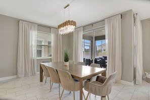 Comedor con una mesa grande, sillas, una araña y vistas a través de un ventanal.