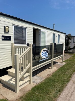 Une caravane située en bord de mer, dotée d’une porte-fenêtre, d’une enseigne et d’un petit espace extérieur aménagé pour s’asseoir.