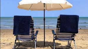 Dos sillas de playa con toallas, una sombrilla blanca y una vista despejada del océano.