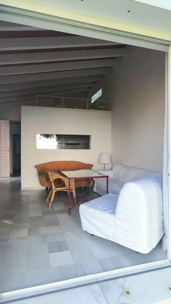 Una sala de estar moderna con un sofá, una mesa y una silla. Hay una ventana sobre la mesa y una lámpara en ella.