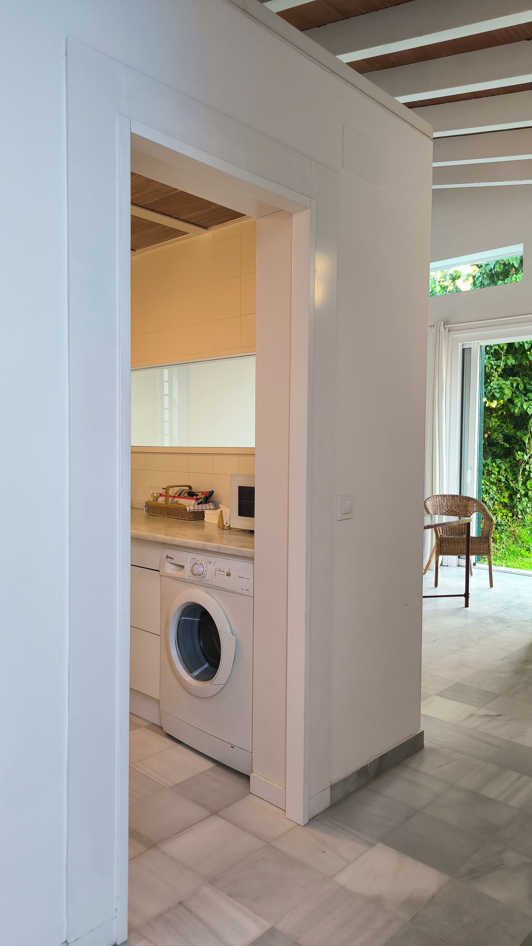 Een wasruimte met een wasmachine, een klein tafeltje met een mand en een stoel.