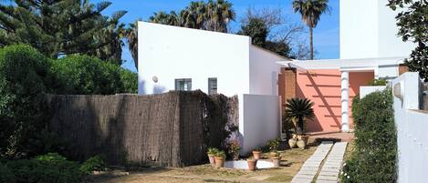 A modern house with a white exterior, a wooden fence, and a garden with potted plants and a palm tree.