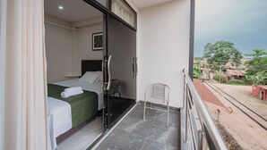 A room with a bed, a chair, and a balcony overlooking a residential area. - KOA LIVING (Pucallpa)