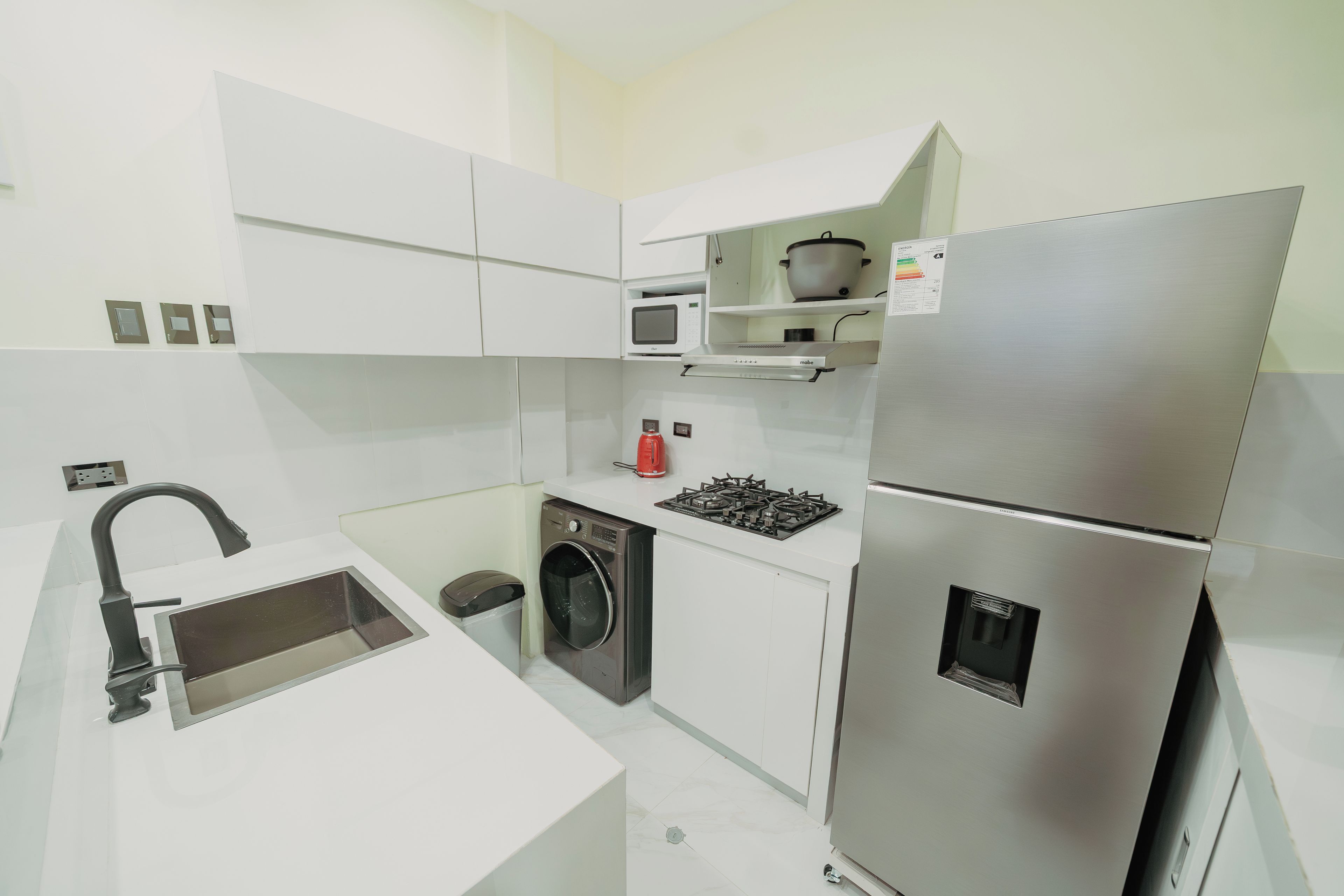 Una cocina moderna con armarios blancos, un refrigerador de acero inoxidable, un microondas, una estufa y una lavadora.