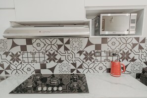 A kitchen with a gas stove, a microwave, and a kettle.