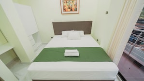 Habitación de hotel con cama, colcha verde, almohadas blancas, un cuadro en la pared y una ventana con vistas.