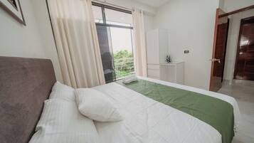 A bedroom with a bed, a window with curtains, a bathroom with a sink, and a door.