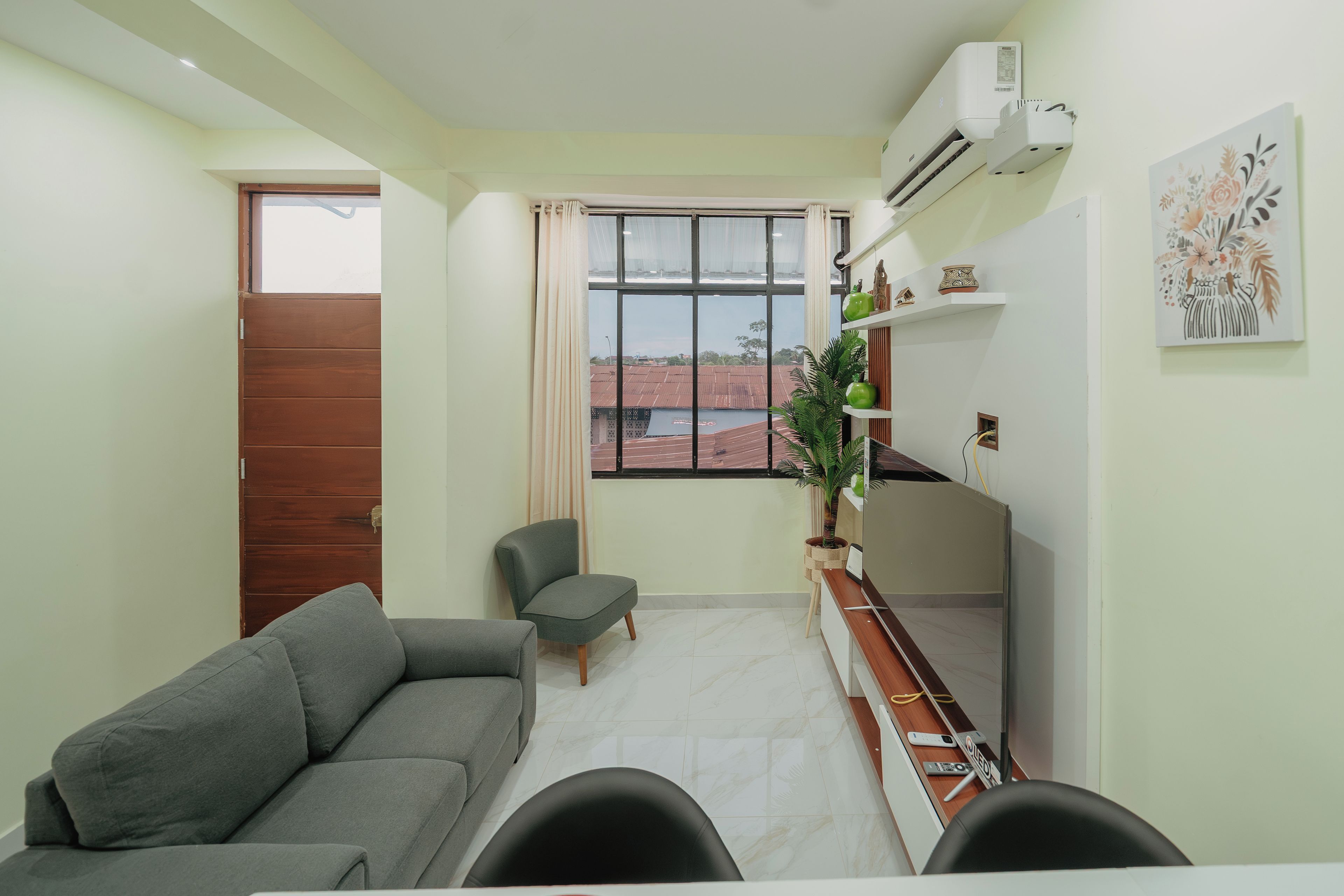 A compact living space with a sofa, a chair, a dining table, and a window with a view of buildings.