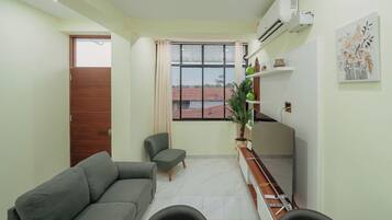 A compact living space with a sofa, a chair, a dining table, and a window with a view of buildings.