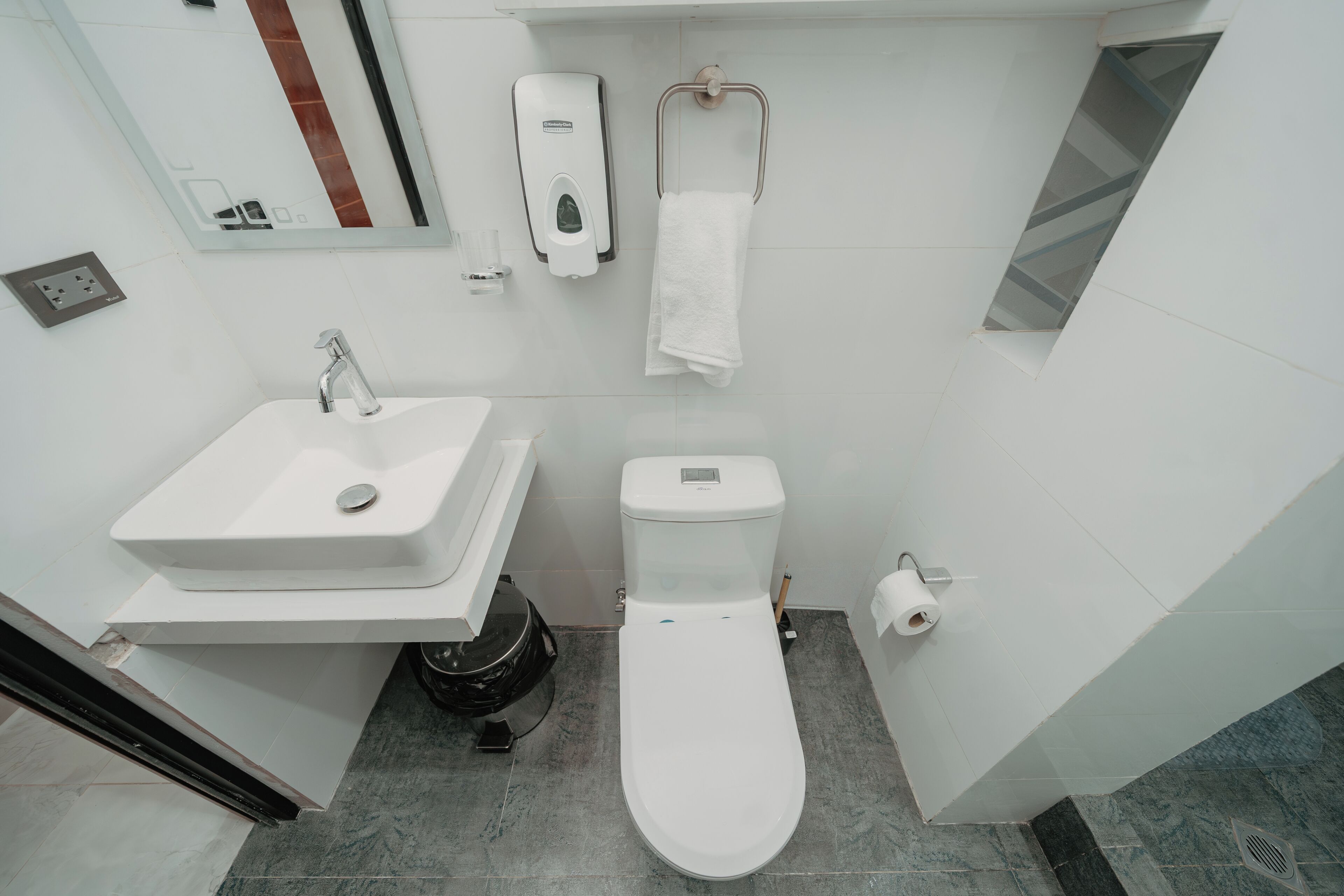 Un baño moderno con lavamanos, inodoro y secamanos blancos.
