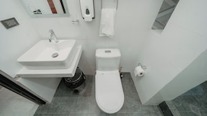 Un baño moderno con lavamanos, inodoro y secamanos blancos.