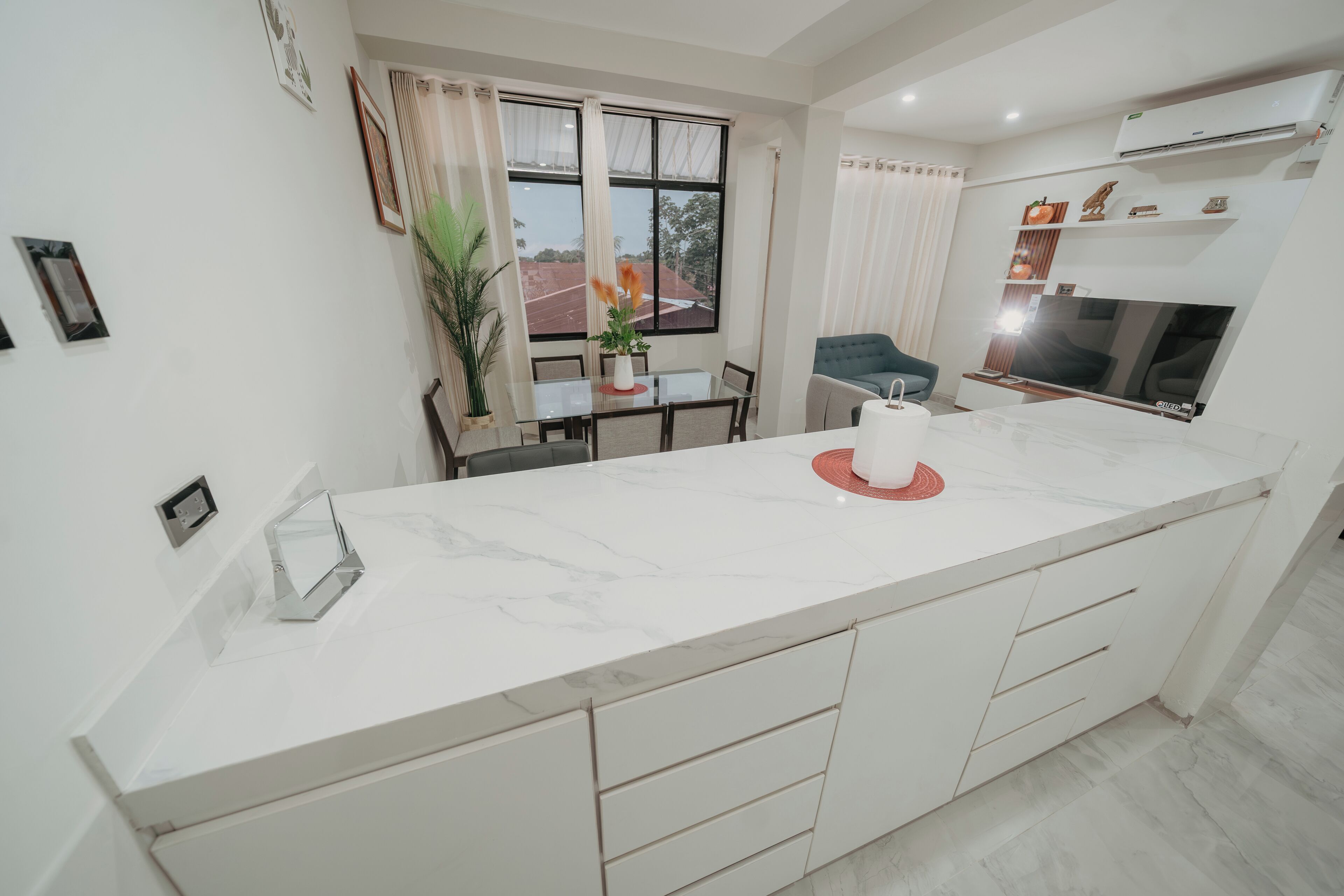 Una cocina moderna con encimera de mármol, un comedor con mesa y sillas, y un amplio ventanal con cortinas.