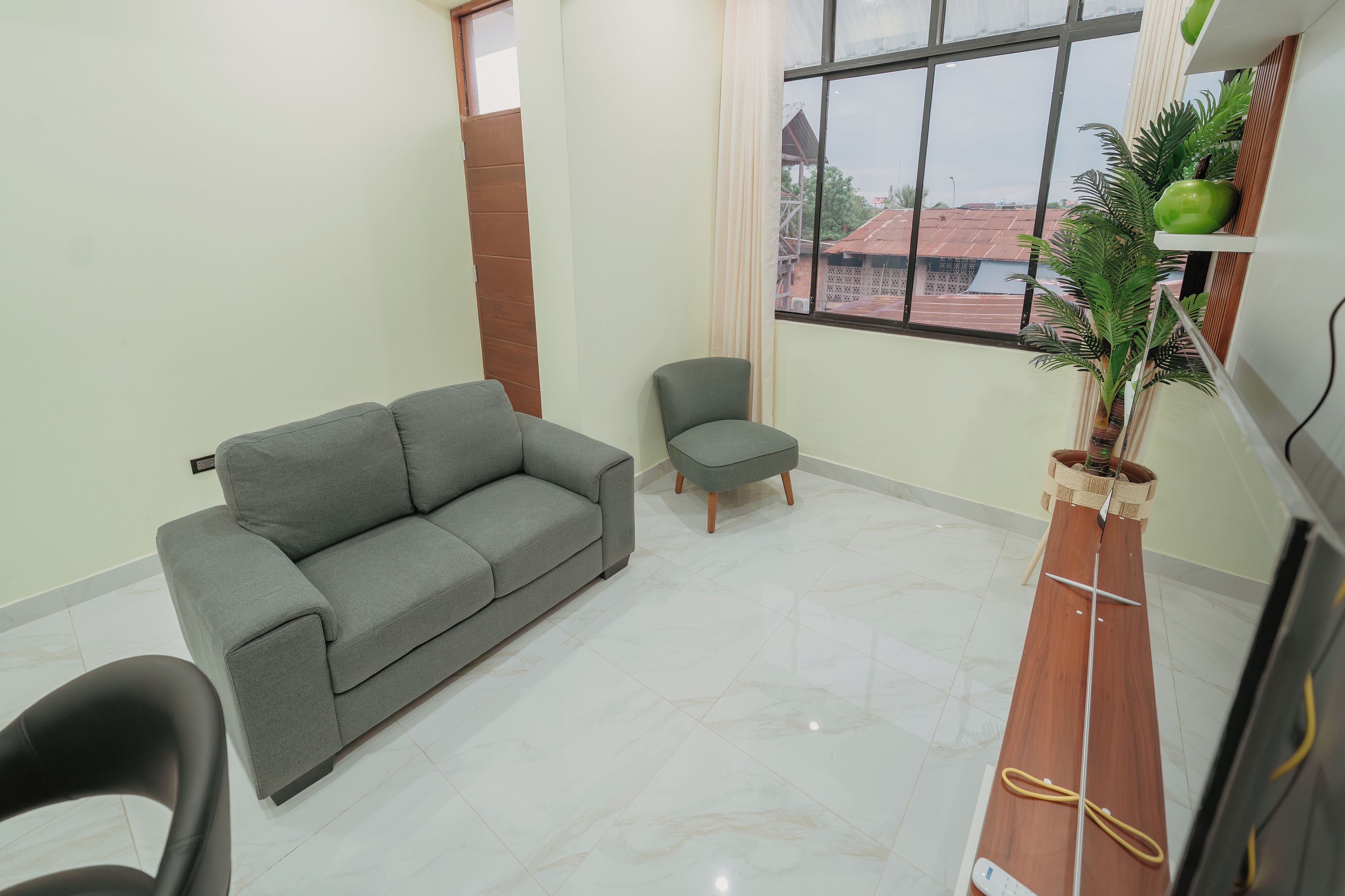 Sala de estar com sofá cinza, uma poltrona pequena e mesa de madeira com uma planta.