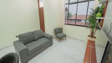 Sala de estar com sofá cinza, uma poltrona pequena e mesa de madeira com uma planta.