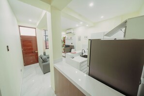A modern kitchen with a refrigerator, sink, and a dining area with a chair.