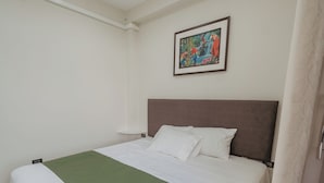 Habitación de hotel con una cama grande, una colcha verde, ropa de cama blanca, un cuadro en la pared y una cortina blanca.