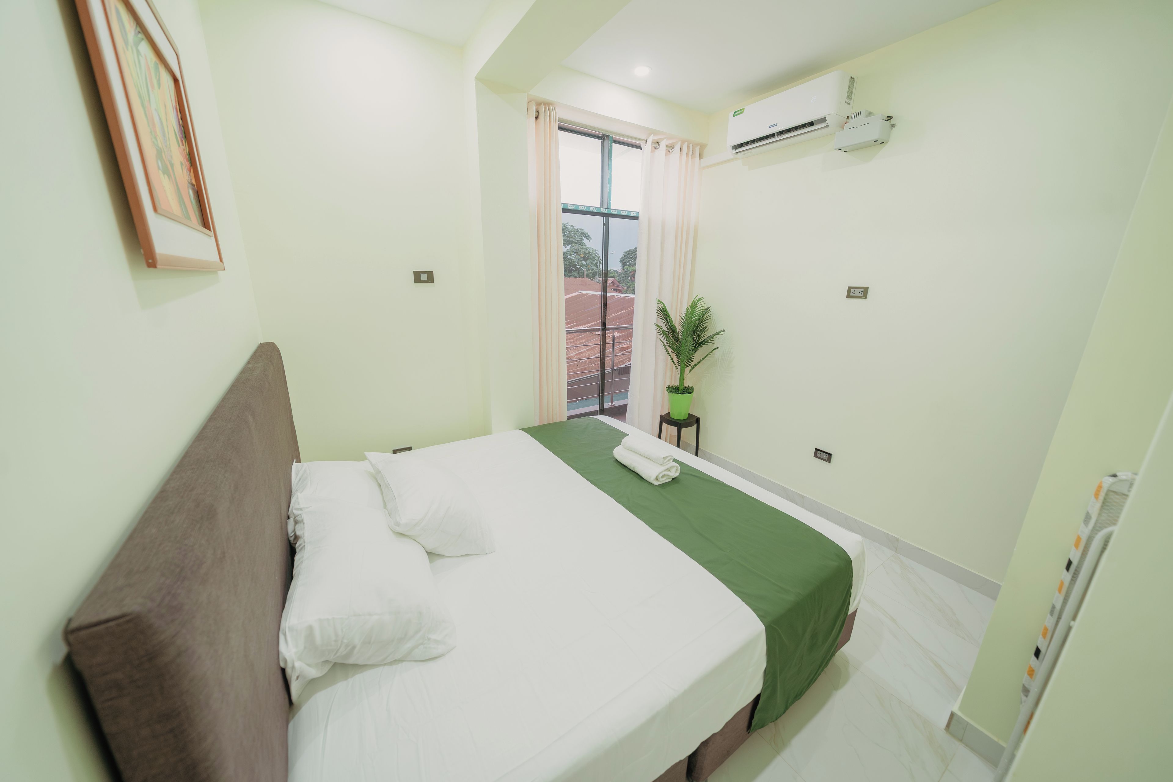 Una habitación de hotel con una cama, una planta en maceta y un equipo de aire acondicionado.