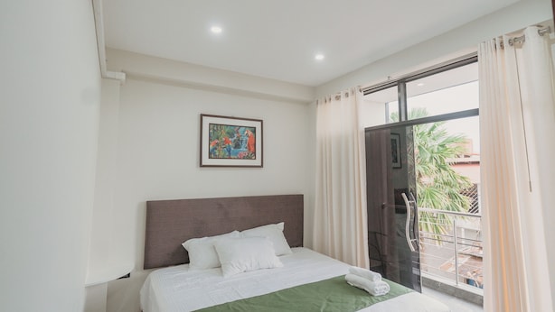 Habitación de hotel con cama, un cuadro en la pared, ventana con cortinas y puerta que da a un espacio exterior.
