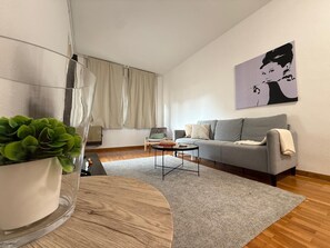 A modern living room with a grey sofa, a small coffee table, a potted plant, and a painting on the wall.