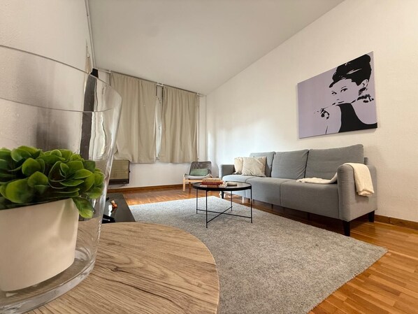 A modern living room with a grey sofa, a small coffee table, a potted plant, and a painting on the wall.