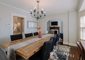 Ein Esszimmer mit einem langen Holztisch, dunklen Stühlen, einer Kristallleuchter und einem Kamin.