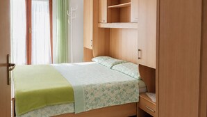 A single bed with a green blanket and floral bedding, a wooden wardrobe, and a window with curtains. - Lovely apartment in Kukljica with WiFi (Kukljica)