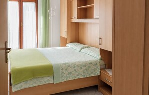 A single bed with a green blanket and floral bedding, a wooden wardrobe, and a window with curtains. - Lovely apartment in Kukljica with WiFi (Kukljica)