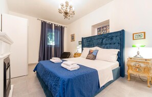 Ein Schlafzimmer mit einem Bett, einer Chandelüster, einem Nachttisch und einem Fenster mit Vorhängen.