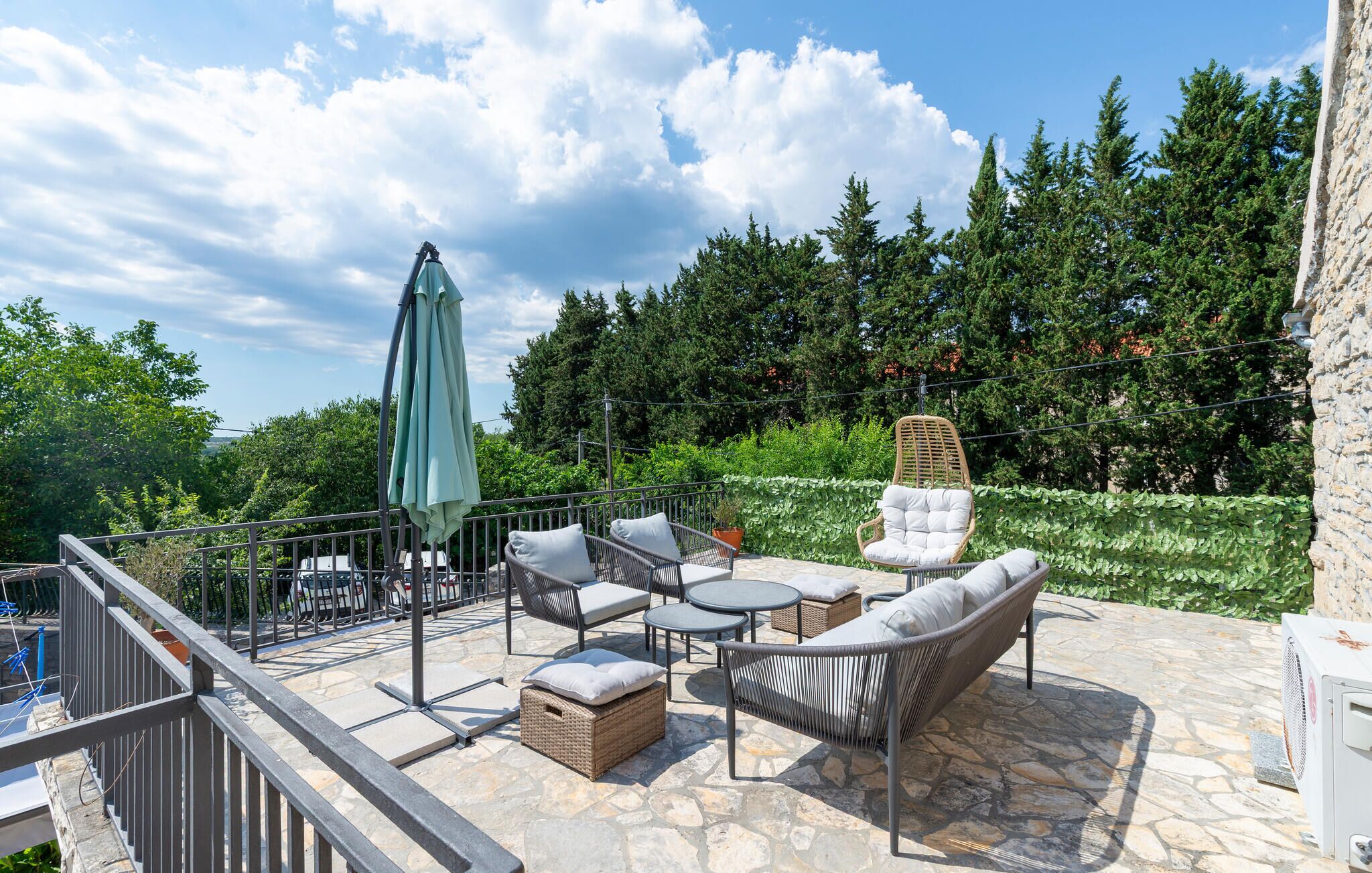 An outdoor patio with wicker furniture, a stone floor, and a view of trees and a stone wall.