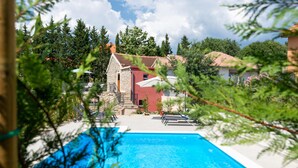 Una piscina con sillones de descanso, un edificio de piedra y follaje circundante.