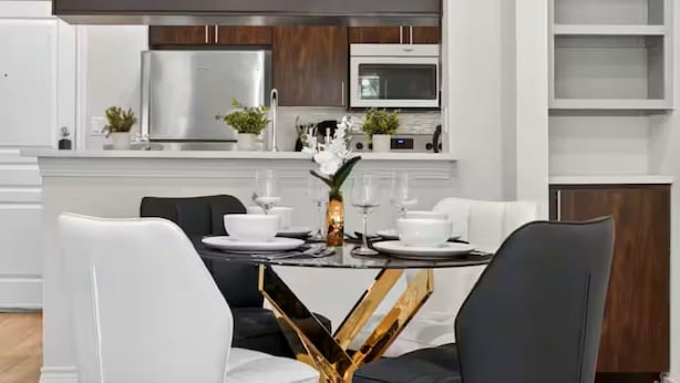 Eine moderne Küche mit weißen Schränken, einem Edelstahl-Kühlschrank, einer Mikrowelle und einem Essbereich mit rundem Tisch und Stühlen.