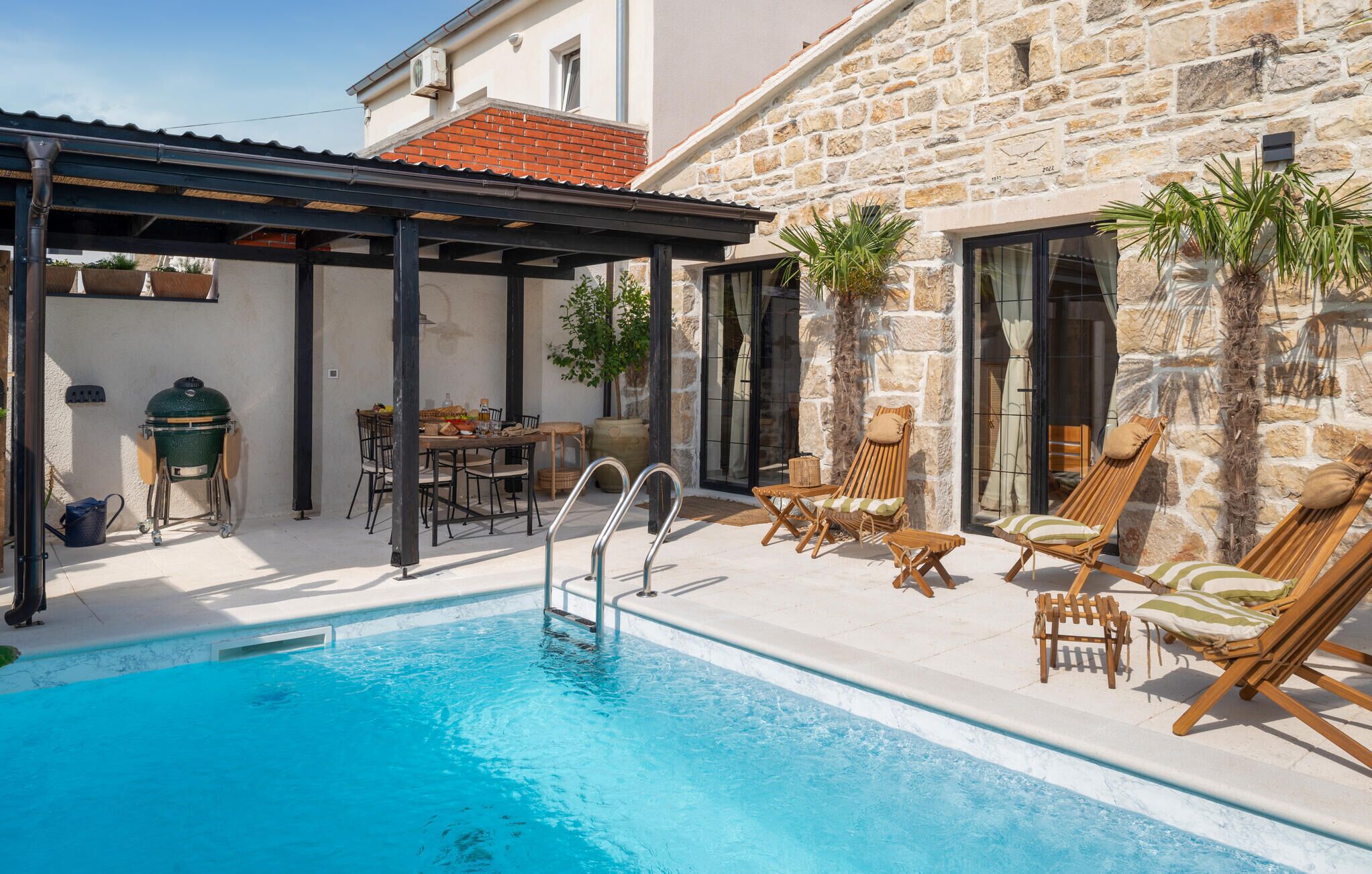 A poolside area with a covered patio, lounge chairs, and a barbecue grill.
