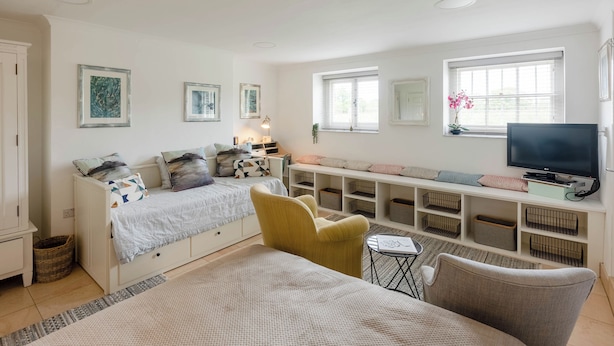 Een slaapkamer met een bed, een gele stoel, een televisie en een plank met opbergbakken.
