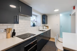A modern kitchen with black cabinets, a white countertop, and a built-in oven. - The perfect Studio (Molesey)