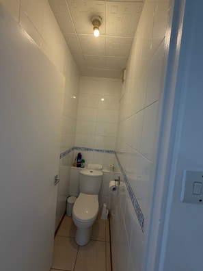 A small, narrow bathroom with a toilet, a sink, and a shower. - Apartment Sleeps 6 With Wifi (Hayes)