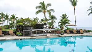 Un espace piscine doté de chaises longues, d’une cascade et de palmiers.