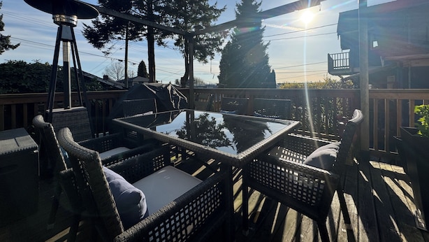 An outdoor deck with wicker furniture, a glass table, and a view of trees and a building. - Vancouver View Home w/ Hot Tub Near Downtown (Vancouver)