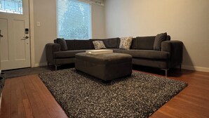A living room with a sectional sofa, an ottoman, a patterned rug, and hardwood flooring. - Vancouver View Home w/ Hot Tub Near Downtown (Vancouver)