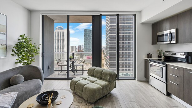 Eine moderne Wohnung mit Sofa, Esstisch, einer Küche inklusive Mikrowelle und einer großen Schiebeglastür, die auf einen Balkon führt.