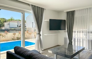 A modern living room with a pool view, a flat-screen TV, and a dining table. - Gorgeous home in Stancija Vergotini (Stancija Vergotini)
