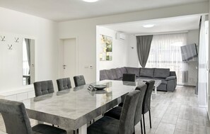 A modern living room with a dining area, grey sofas, a large dining table, and a large window with curtains. - Stunning home in Stancija Vergotini (Stancija Vergotini)