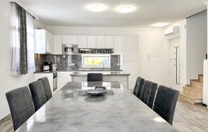 A modern kitchen with white cabinets, a microwave, and a stove. There is a dining table with chairs and a coffee maker. - Stunning home in Stancija Vergotini (Stancija Vergotini)